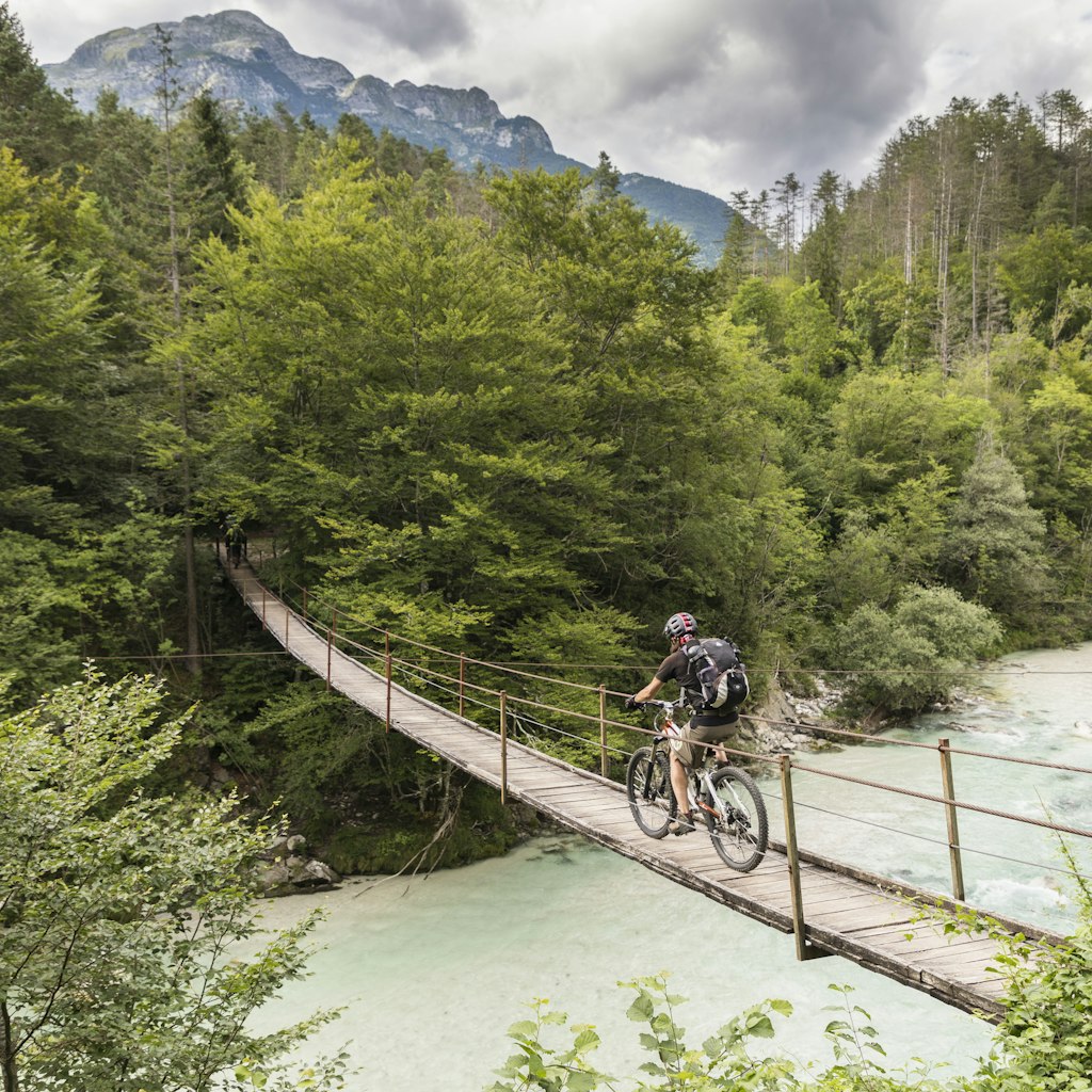 Male mountain biker crossing a suspension bridge over the Soča River in the Julian Alps of northern Slovenia.