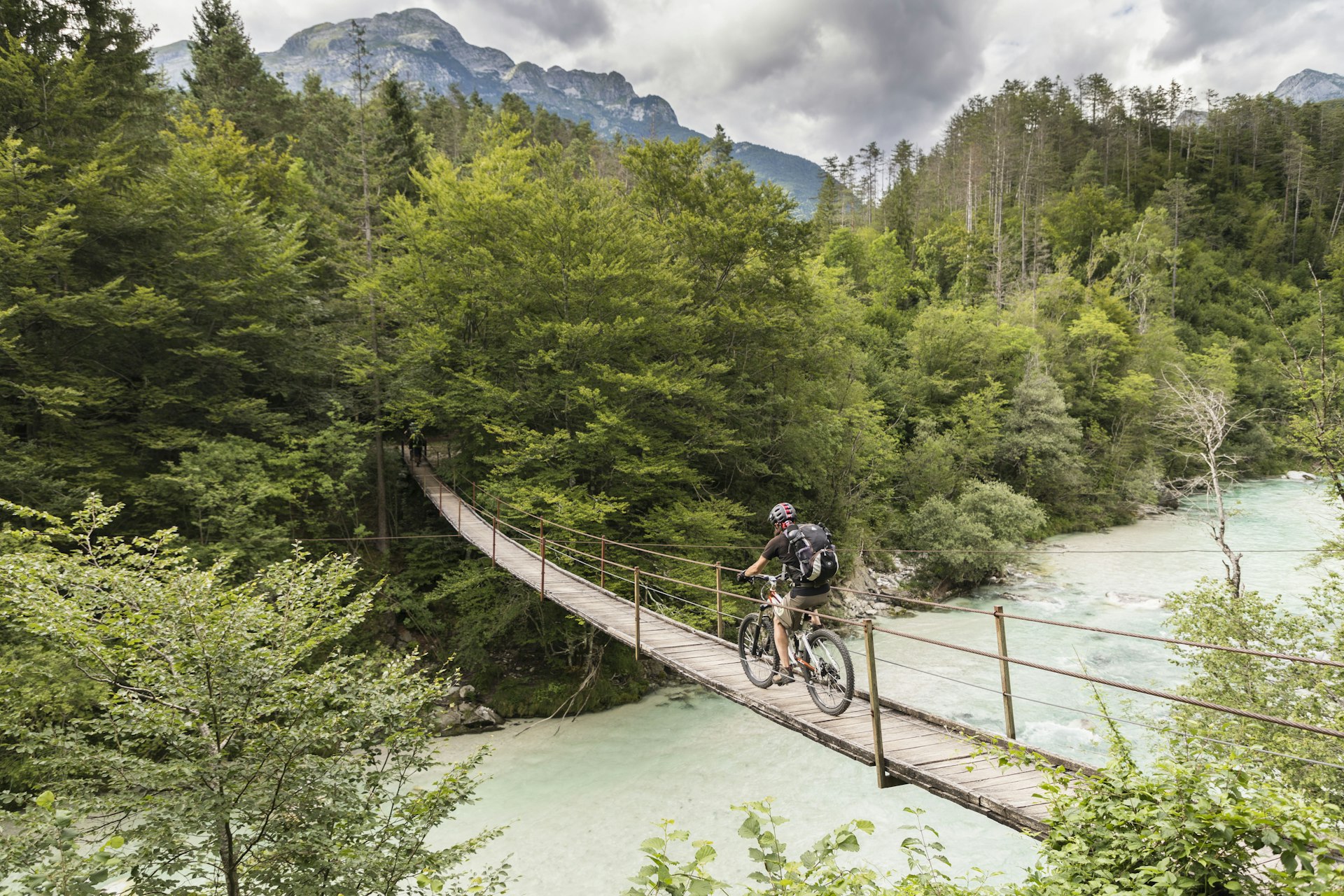 Male mountain biker is crossing a suspension bridge over rapids in the mountains of Slovenia
