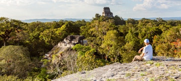 Tourist looking at old mayan ruins from high lookout (Temple IV and temple of the Lost World), Tikal National Park, Peten, Guatemala