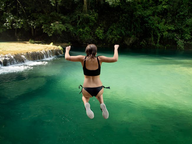 Rear view of woman jumping into a pool against trees in Semuc Champey, Guatemala