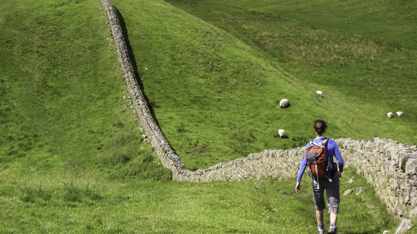 A hiker walking alongside Hadrians Wall near Crag Lough in Northumberland, England