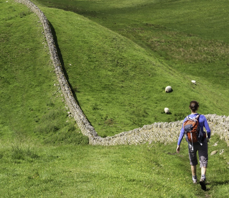 A hiker walking alongside Hadrians Wall near Crag Lough in Northumberland, England