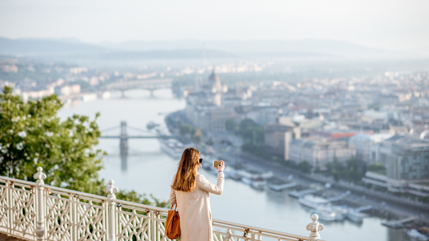 Young woman photographing beautiful morning view on Budapest city from the Gellert hill in Hungary