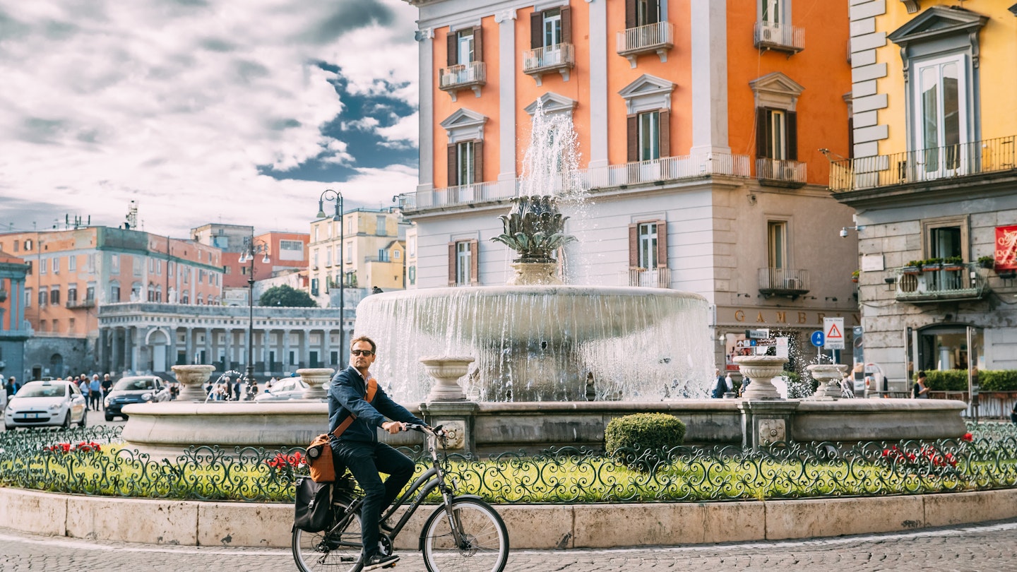 Naples, Italy - October 17, 2018: Adult Caucasian Man Tourist Riding On Bicycle Near Fontana del Carciofo.