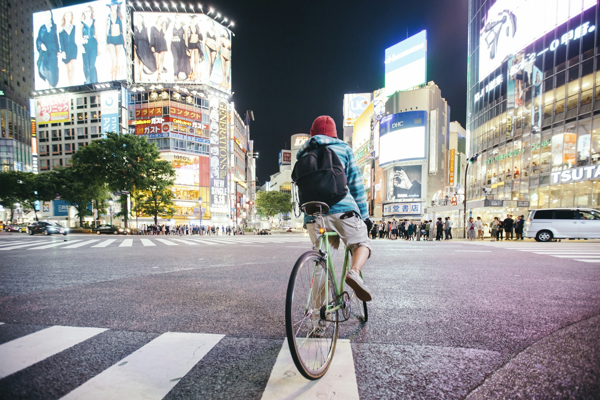 Young guy with backpack riding a bike at evening time on Shibuya crossing in Tokyo, Japan
