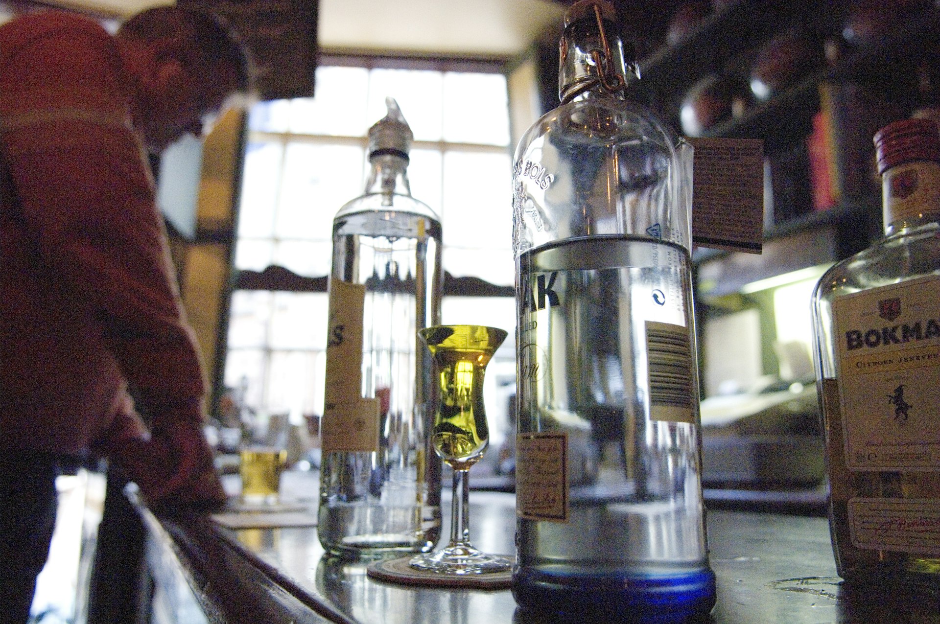 Bottles of Dutch gin and a glass of yellow gin pictures on the bar at De Drie Fleschjes