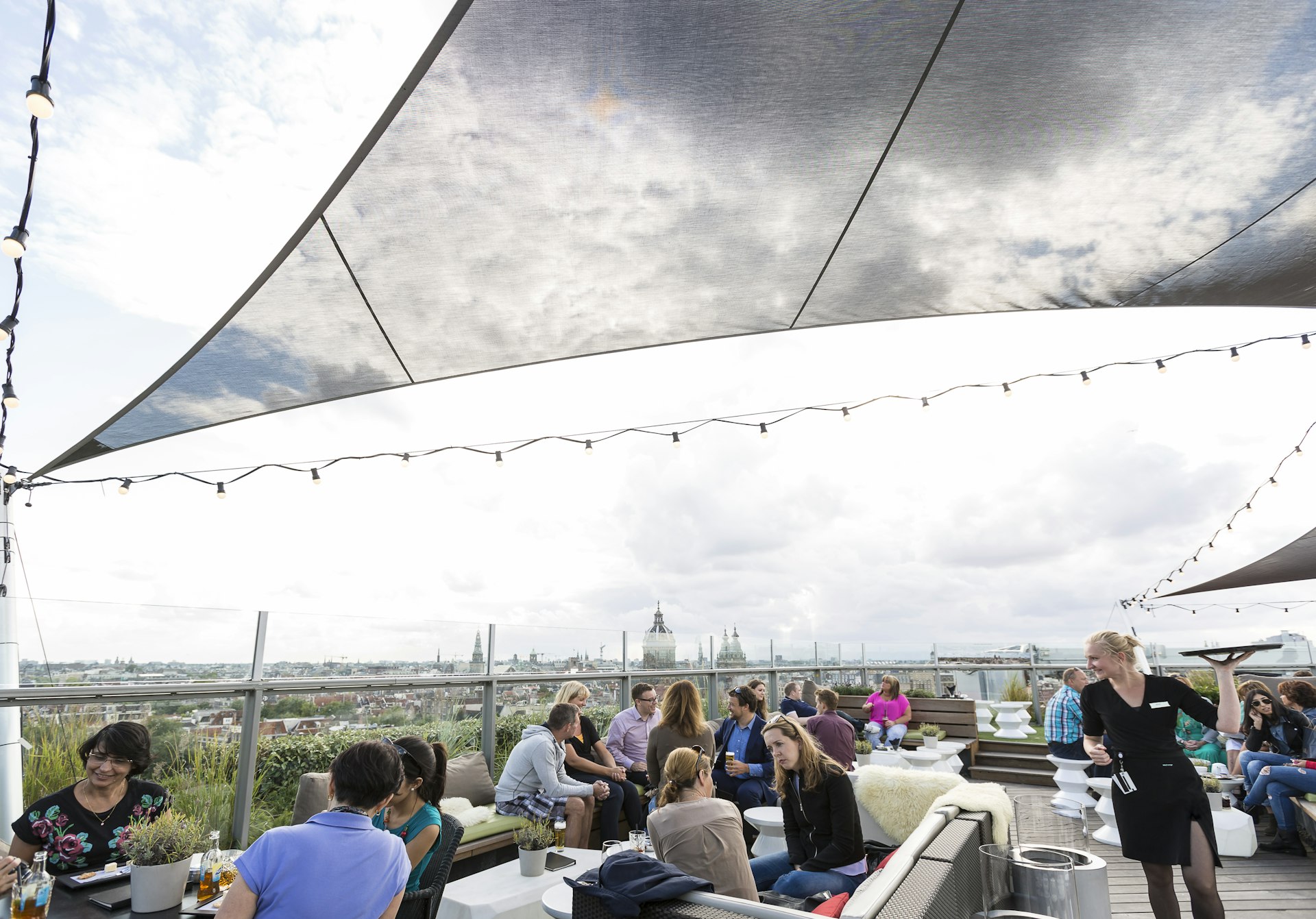 Patrons sitting outside on the rooftop bar at SkyLounge, Amsterdam, under a cloudy sky