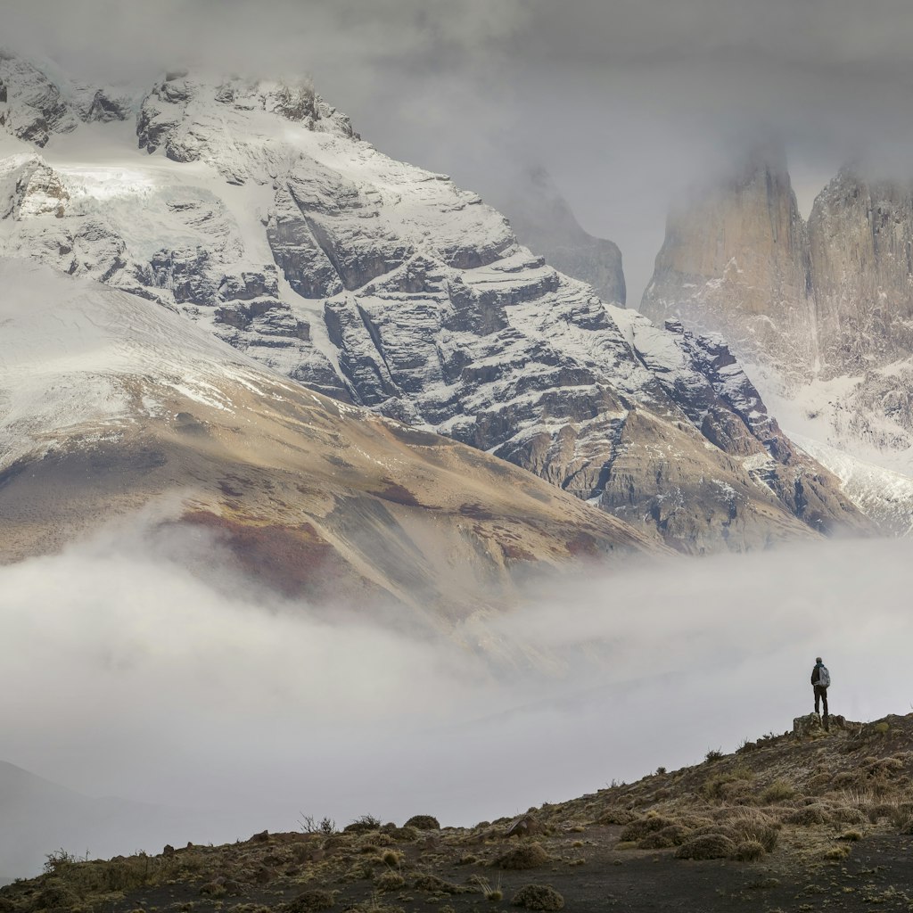 A hiker stands in awe of the huge granite peaks of the three Torres del Paine, part of the larger range of the Cordillera Paine.