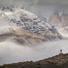 A hiker stands in awe of the huge granite peaks of the three Torres del Paine, part of the larger range of the Cordillera Paine.