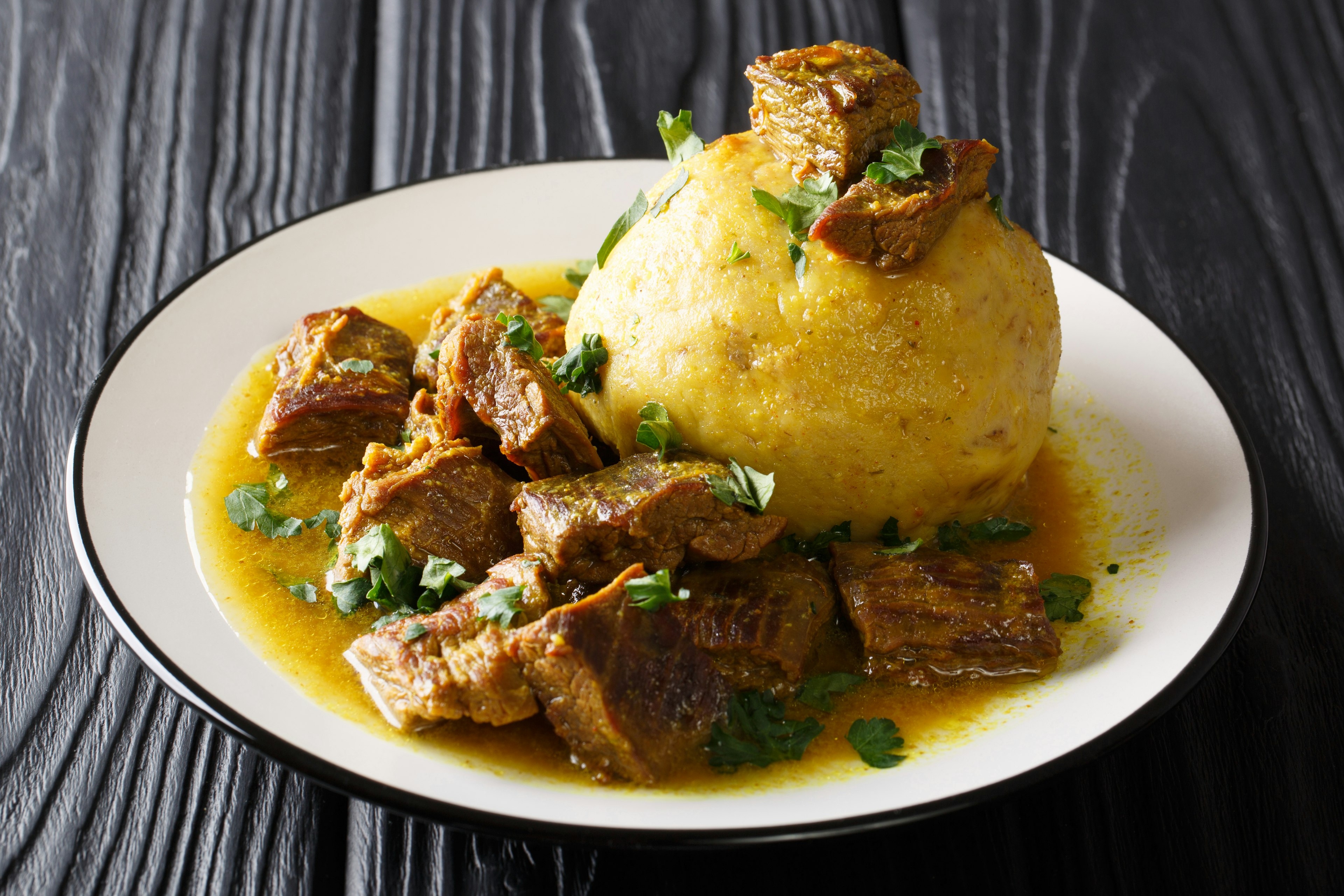 Closeup of a plate of spicy mofongo topped with chicharron and served next to meat and broth.  