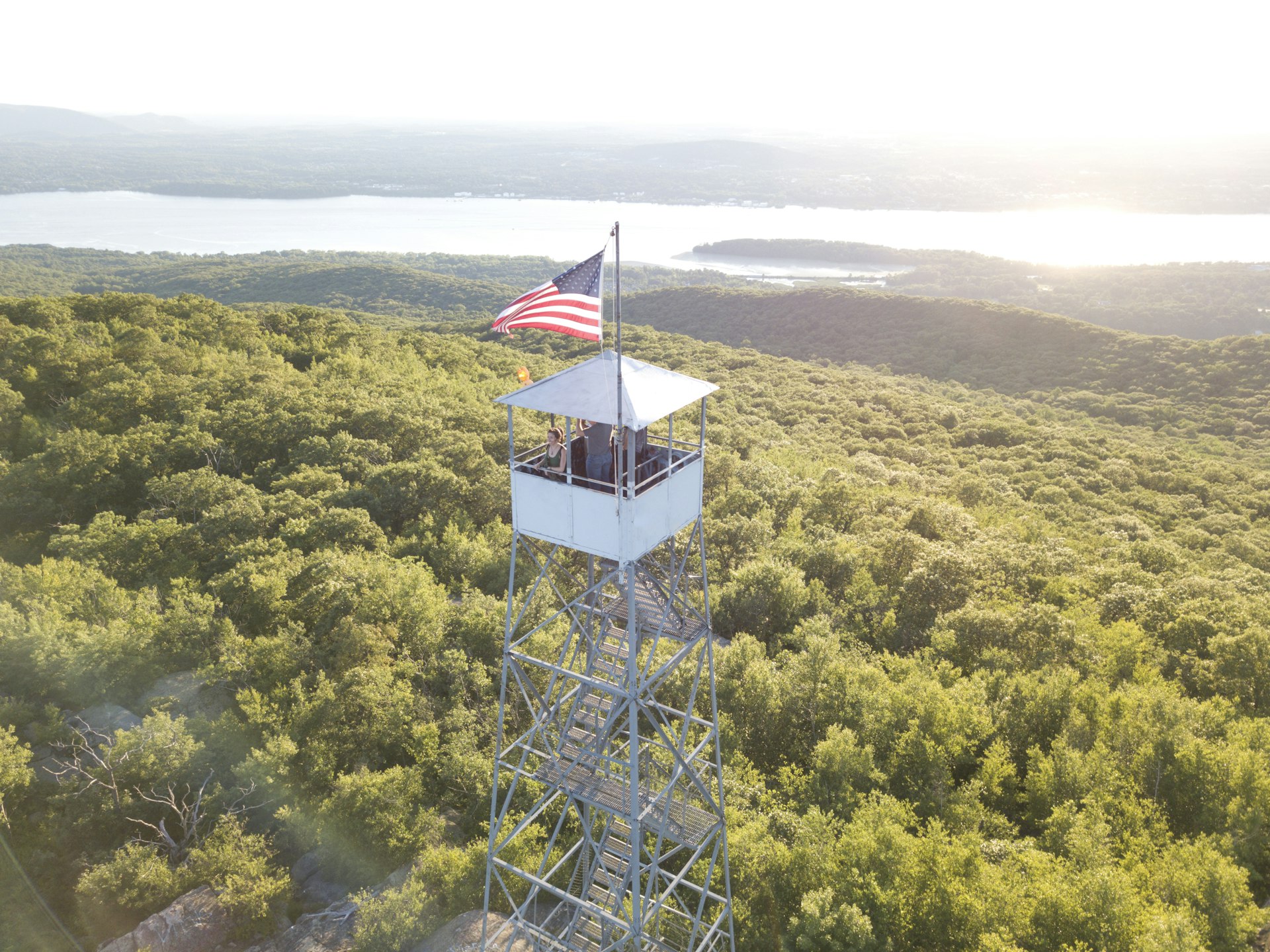 A woman in a tower with an American flag, looking out over the Hudson River, greenery and mountains
