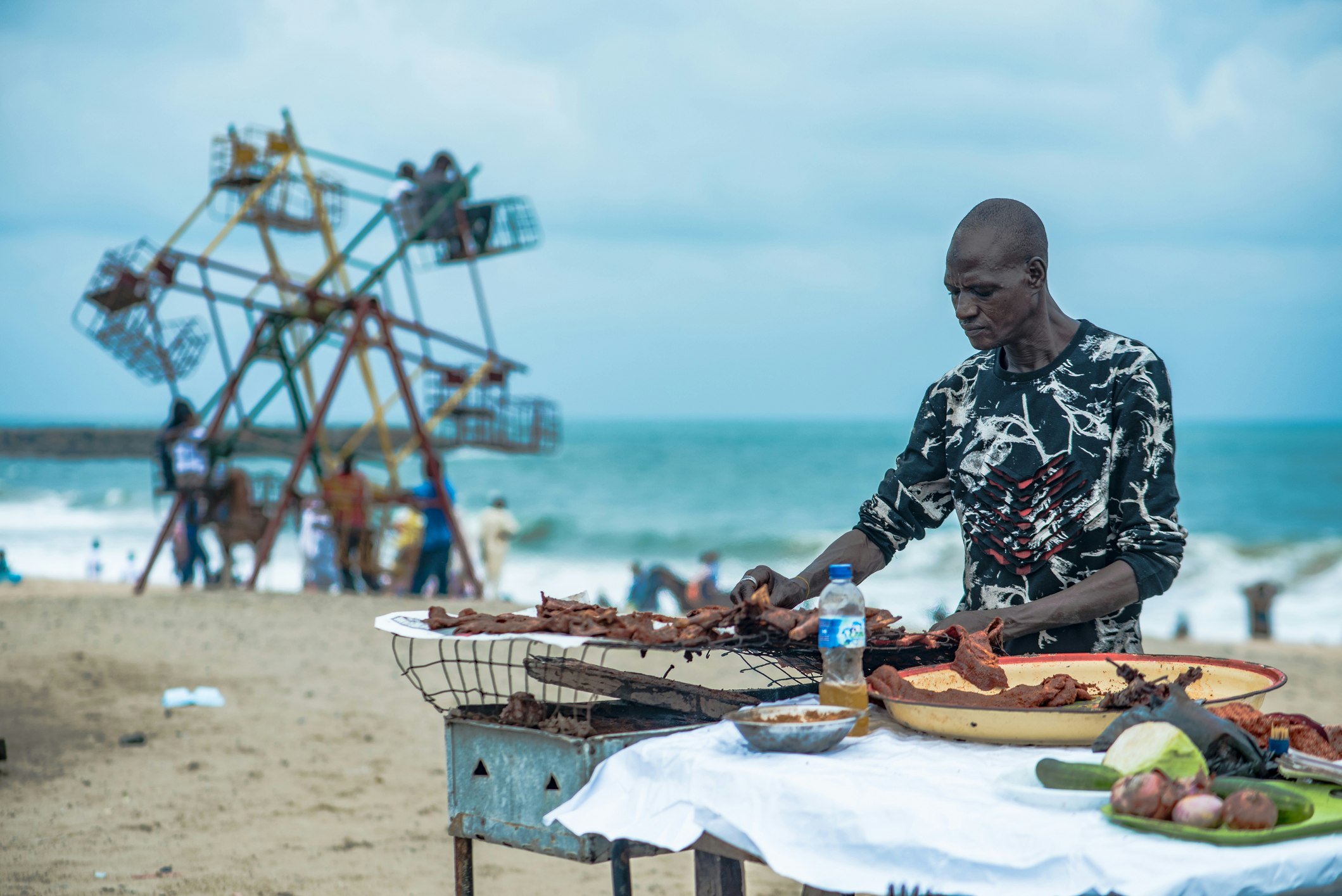 A man preparing roasted suya at a street food stall by the beach