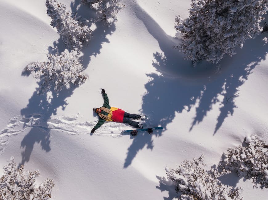 Vinter flygfoto porträtt av en kvinnlig snowboardåkare liggande i ren snö mellan granar