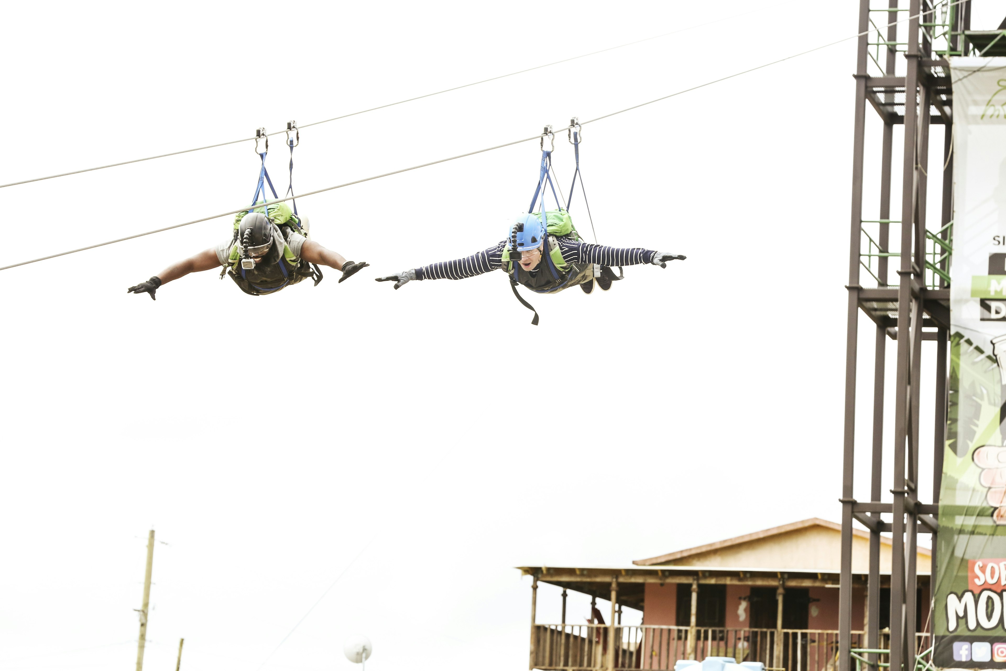 Two men spread their arms while zip lining down a tall line.