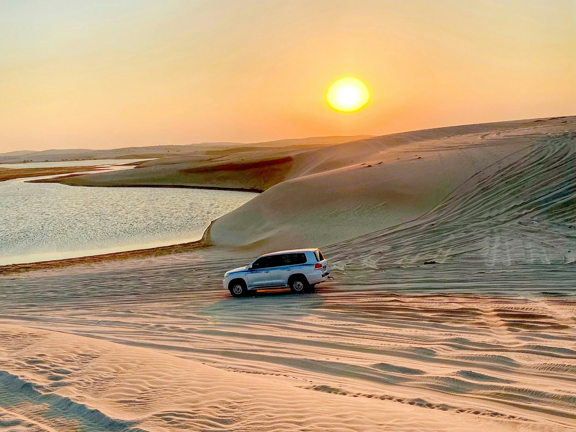 A 4WD on the sand dunes approaching a very still lake