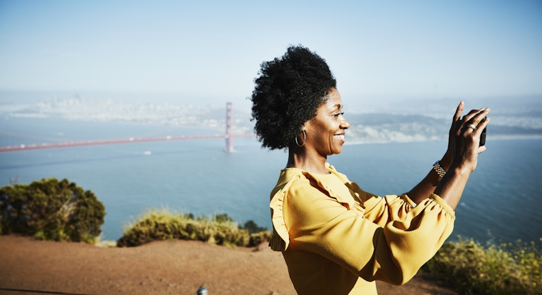 A black woman smiling and taking a picture of San Francisco with the Golden Gate Bridge in the background