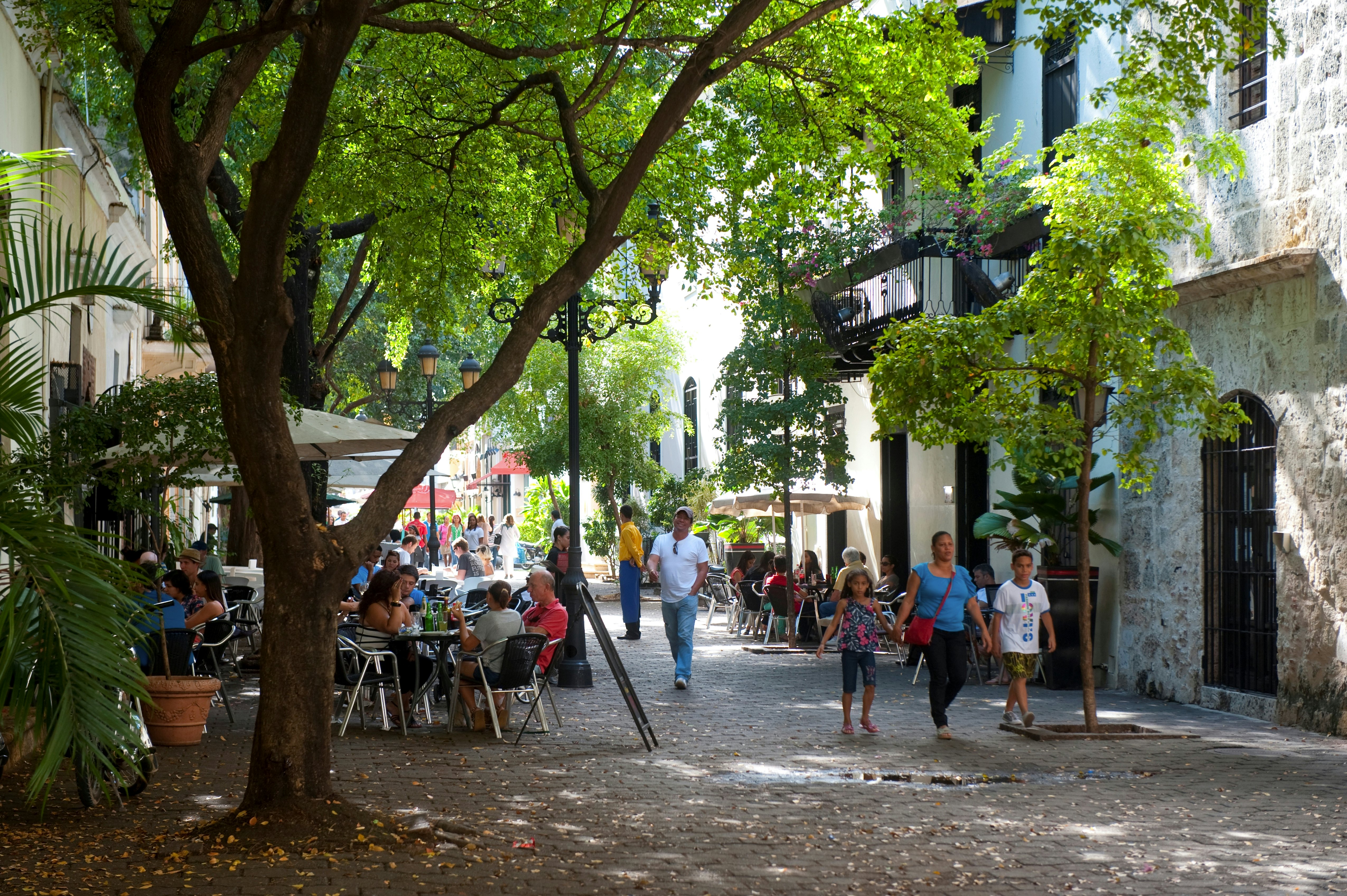 Groups of people relax at tables, while others stroll on the cobble stone streets of Zona Colonial in Santo Domingo, DR.