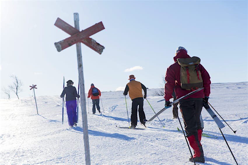 Four people dressed in brightly colored ski gear walk up the slope as they practice cross-country skiing