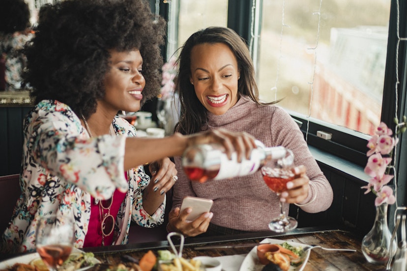 Two women are enjoying a meal in a restaurant with rose wine. They have prawns and a sharing platter in front of them.