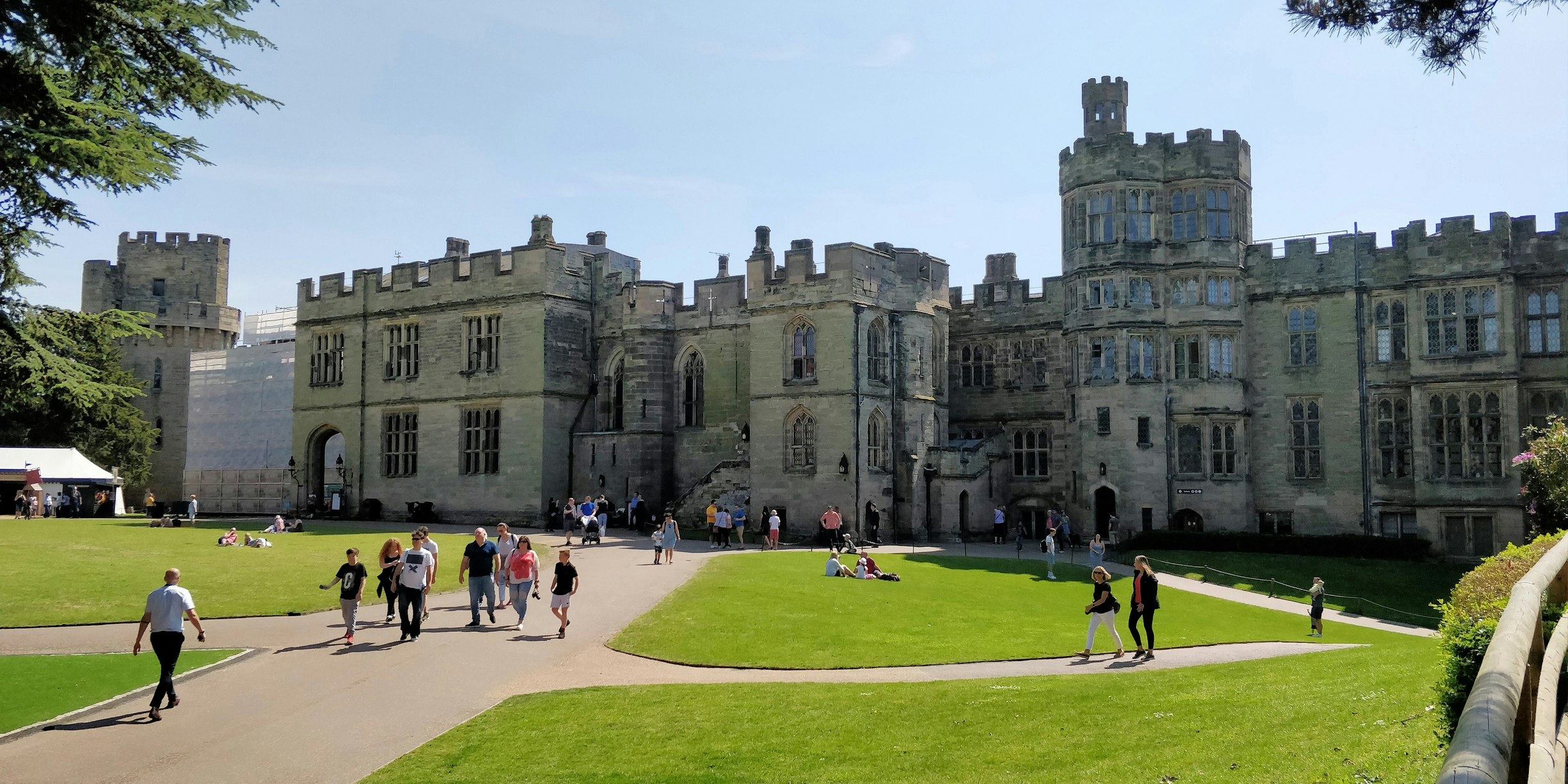 People explore the beautiful grounds of a large castle with turrets and huge stone battlements