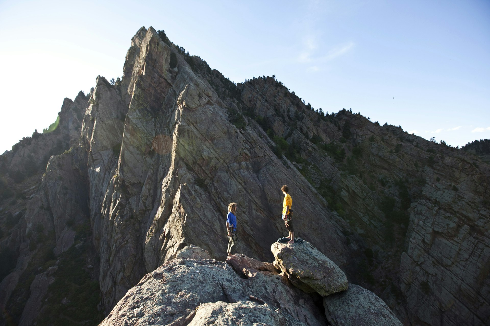 Two young men stand triumphantly on top of a huge rock that they have climbed
