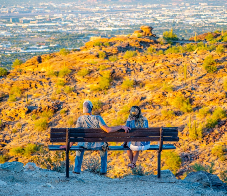 A young man and woman watch the sun go down Phoenix, Arizona from Dobbins Lookout on South Mountain.