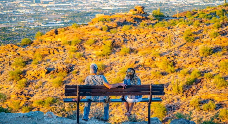 A young man and woman watch the sun go down Phoenix, Arizona from Dobbins Lookout on South Mountain.