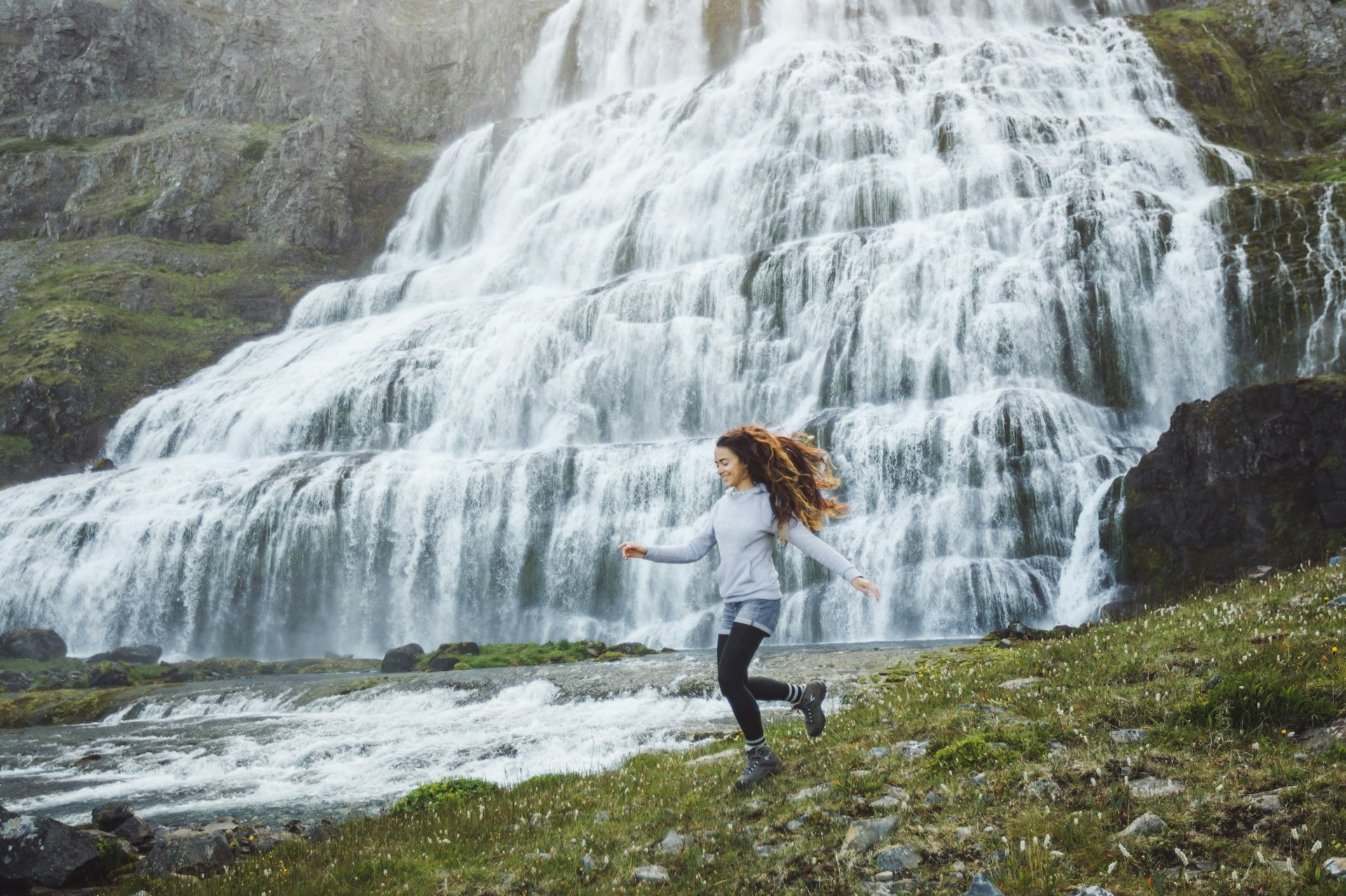 Young happy woman enjoying view of Dynjandi waterfall. Breathtaking view of famous icelandic waterfall in Westfjords