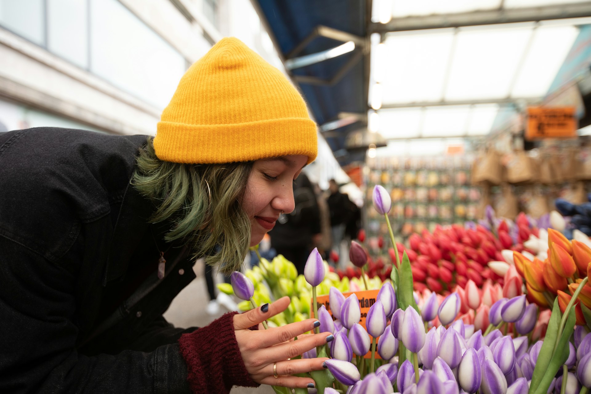 A woman wearing a yellow hat leans in to smell a bunch of tulips