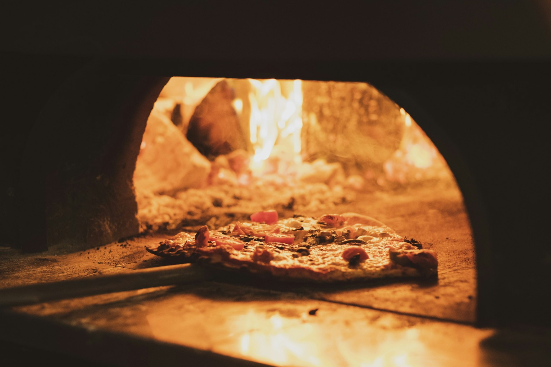 A large wooden shovel pushes a pizza pie into a wood-burning stove.