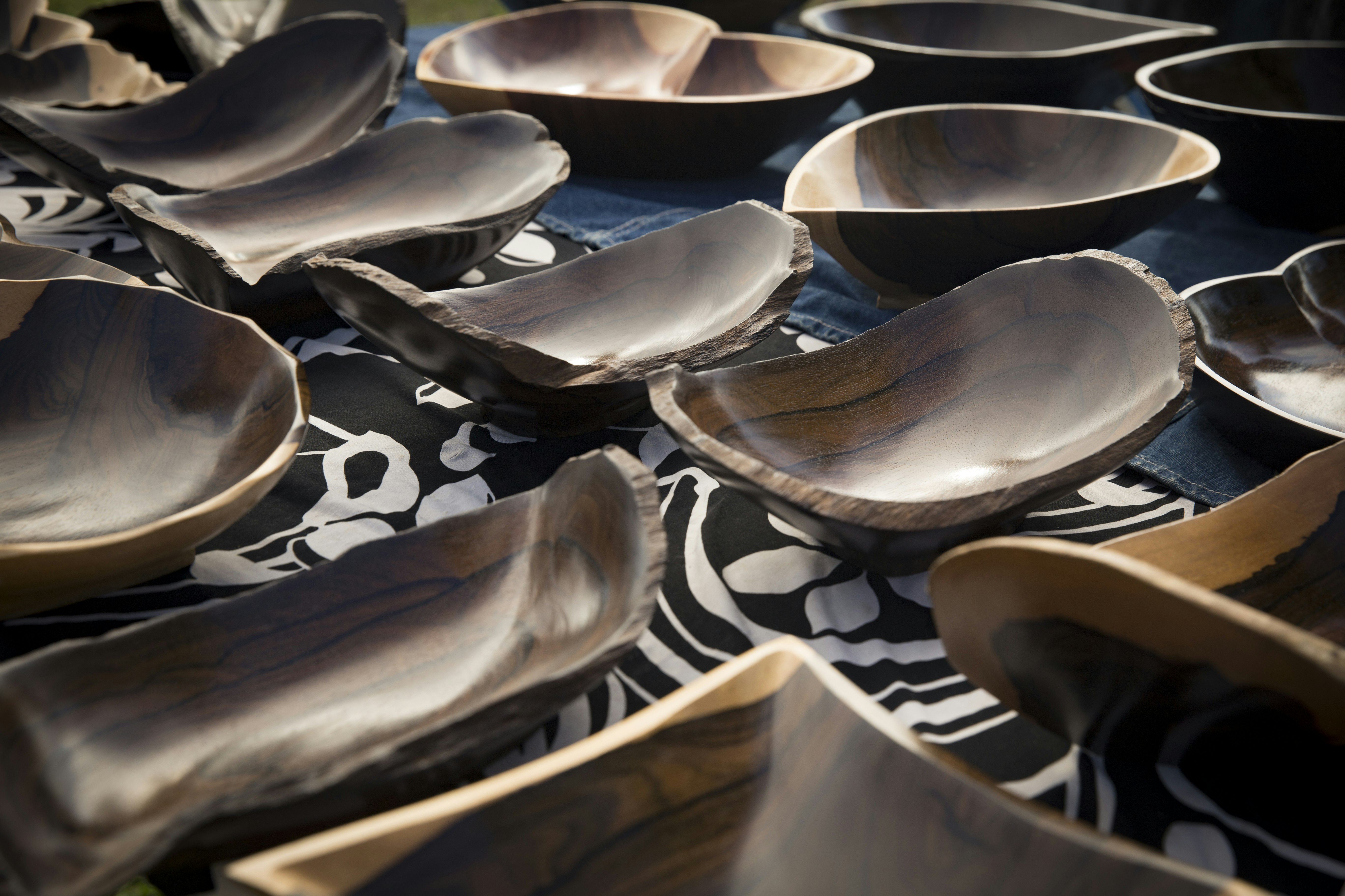A collection of handmade wooden souvenir bowls are placed on a blue, black and white table cloth.