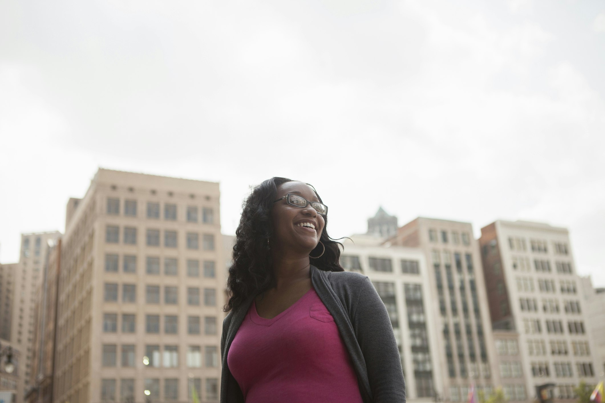 Low-angle portrait of a smiling woman with Detroit high-rises in the background