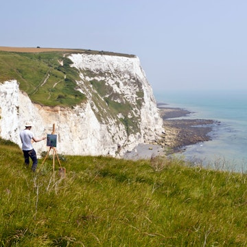 An artist painting the coastline of the Dover Cliffs from the top of the chalky hill, Dover, United Kingdom.