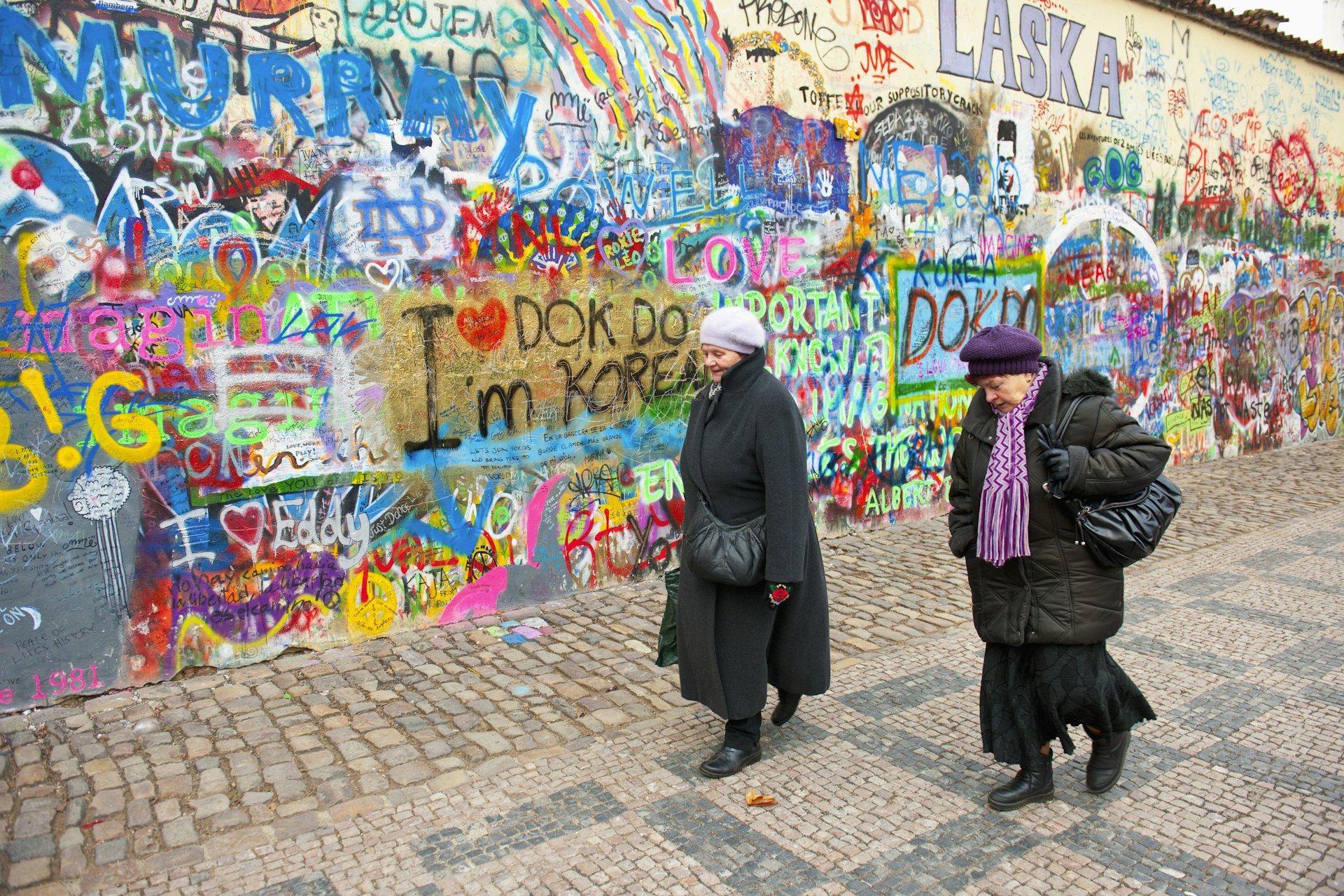 Two people walk along a graffiti-lined cobbled street