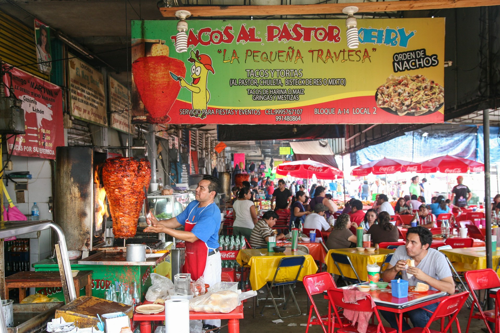 A man carves meat for tacos al pastor among crowded tables at the Mercado Municipal Lucas de Gálvez market in Mérida