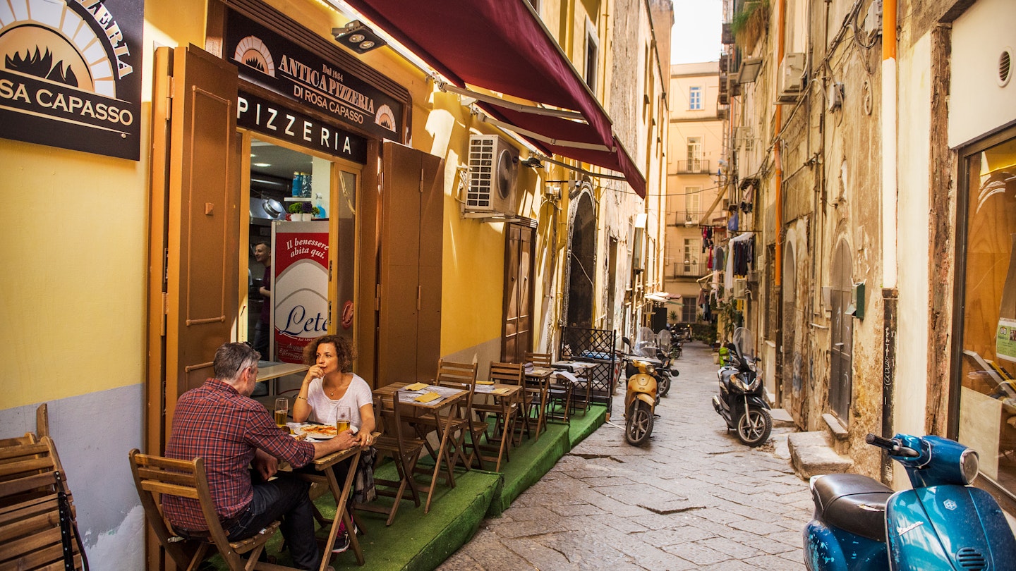 April 19, 2018: A couple eating pizza outside a pizzeria in the old city of Naples.