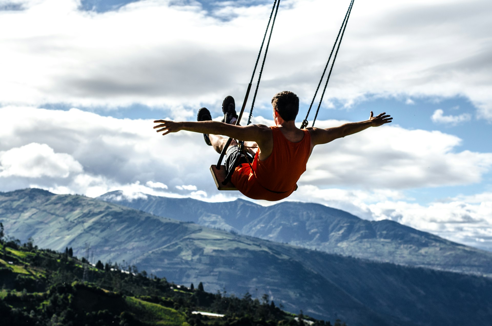Man swinging on the 'Swing at the End of the World' with mountains in the distance. 