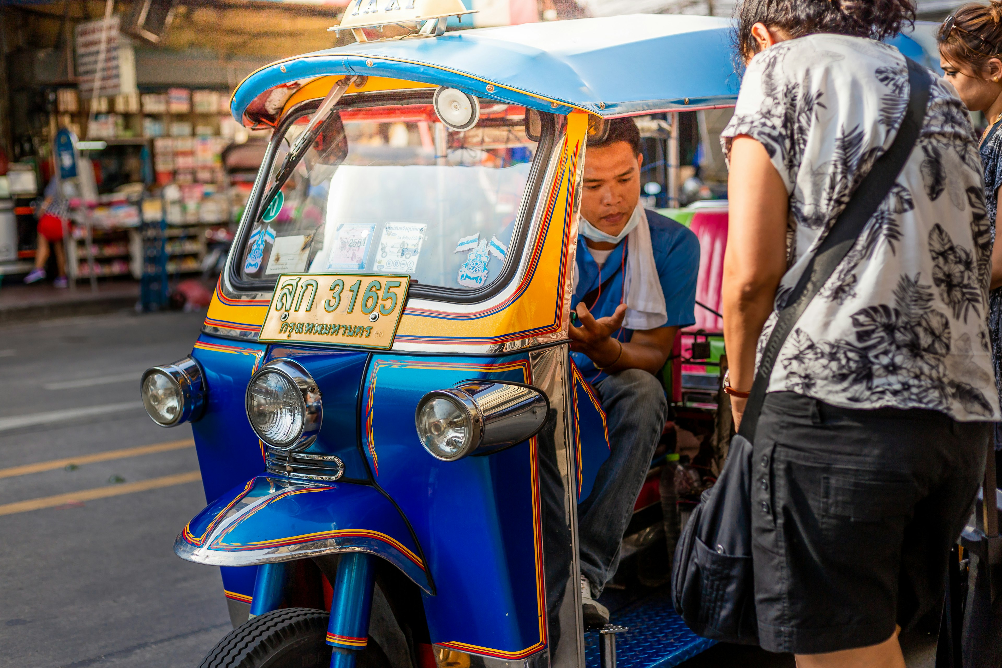 A driver in a blue and white tuk-tuk, picking up a passenger