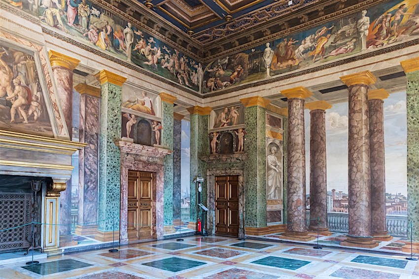 An opulent marble checkerboard floor, marble columns and ornately frescoed walls in an interior at Villa Farnesina, Roma