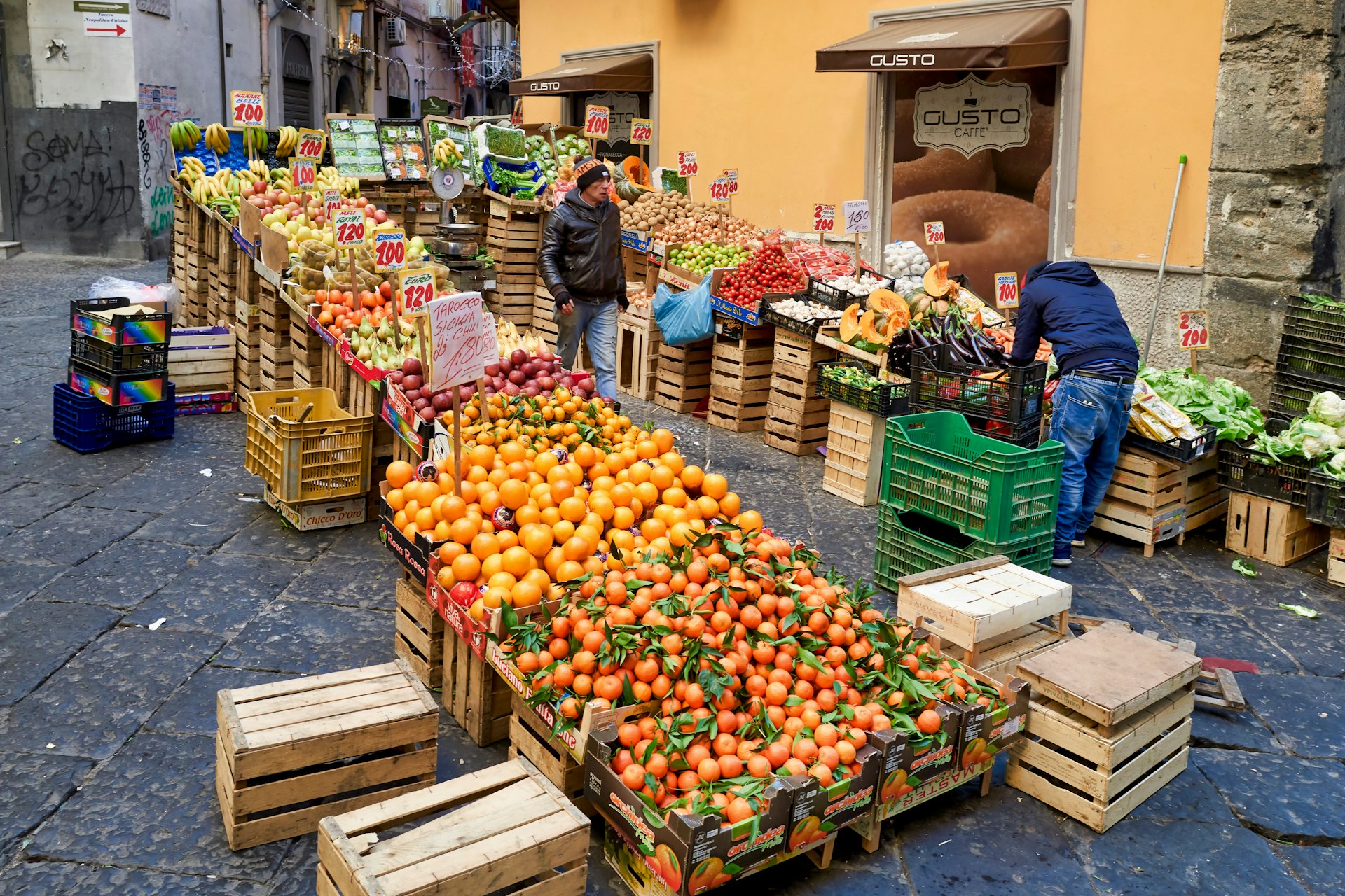 A wide shot of oranges and other produce stacked high at a greengrocer in La Pignasecca market quarter, Naples