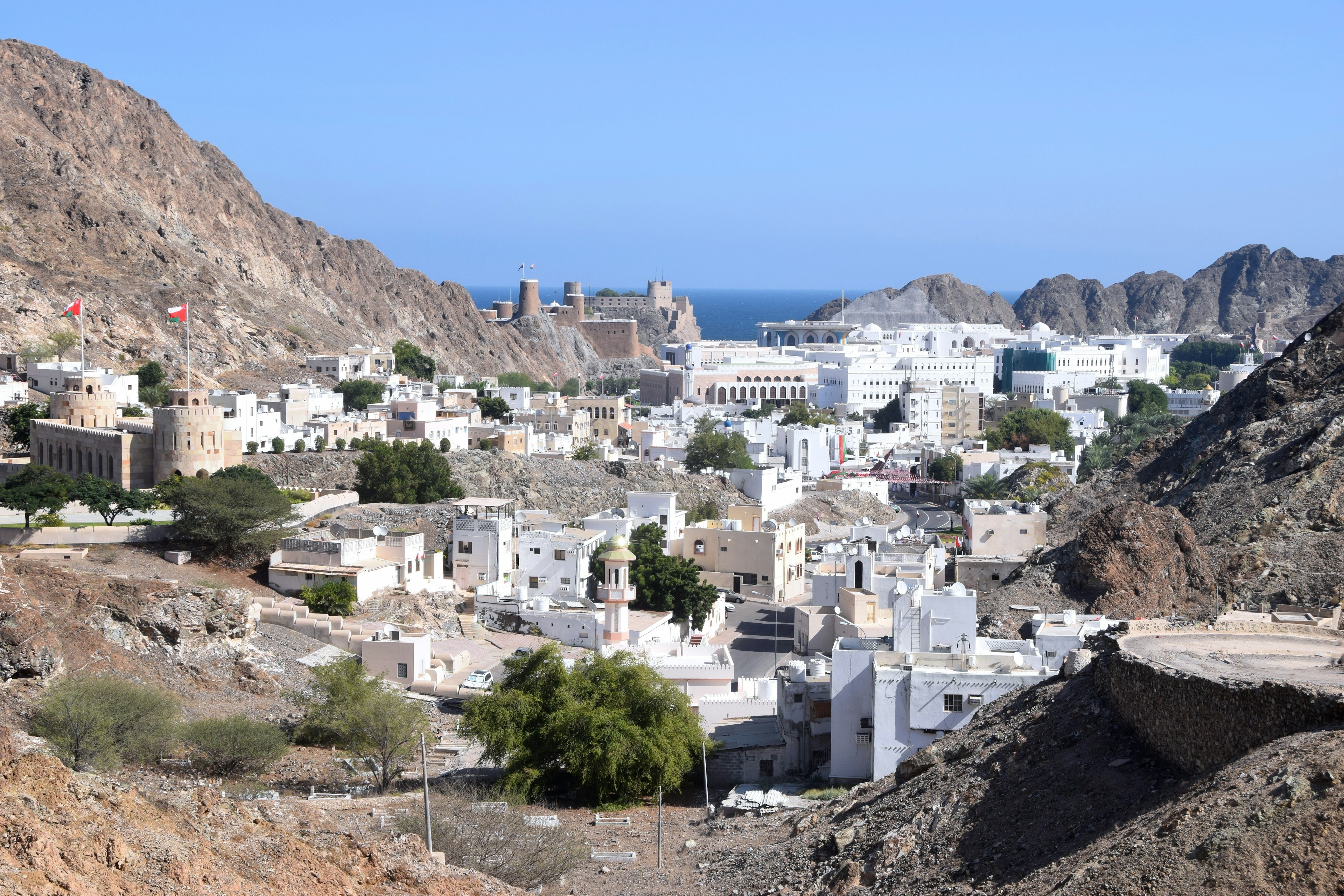 View of the white buildings of the old town of Muscat, Oman, among brown mountains and the blue Gulf of Oman in the distance