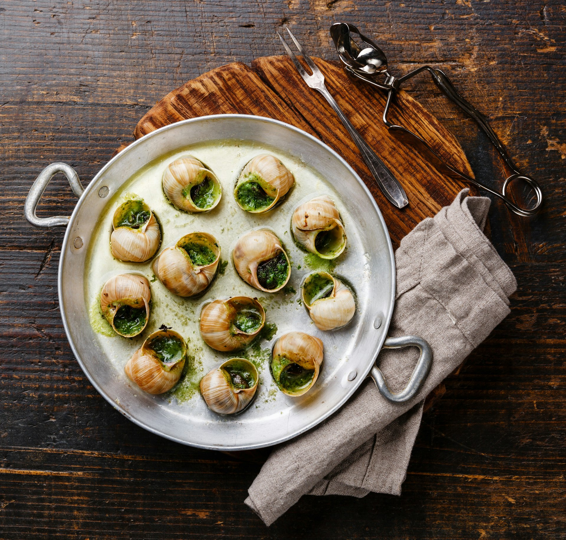 An aluminum pan of escargots de Bourgogne snails with garlic, herbs and butter in on rustic wooden table