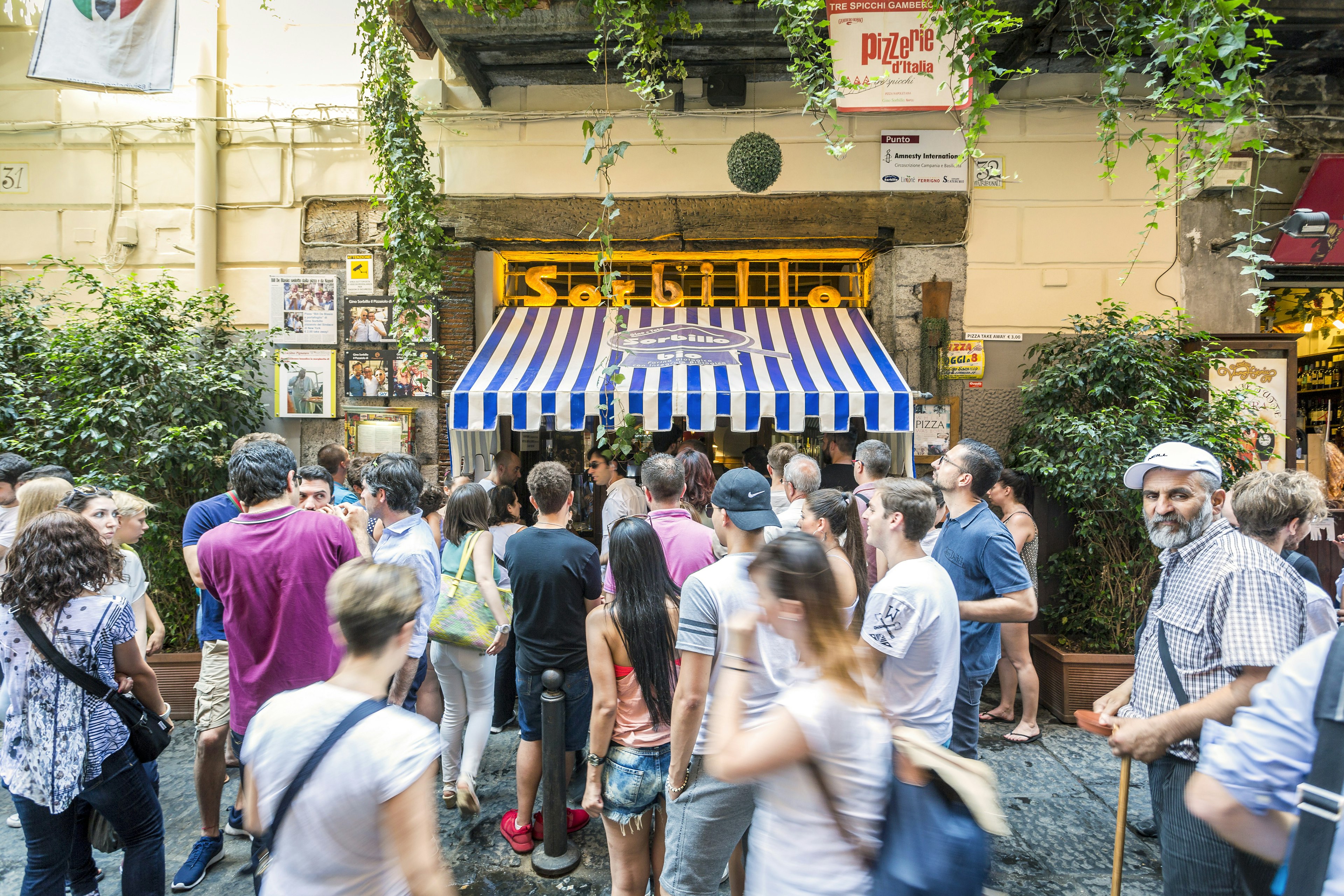 A crowd forms in front of the blue awning of Gino Sorbillo Pizzeria in Naples