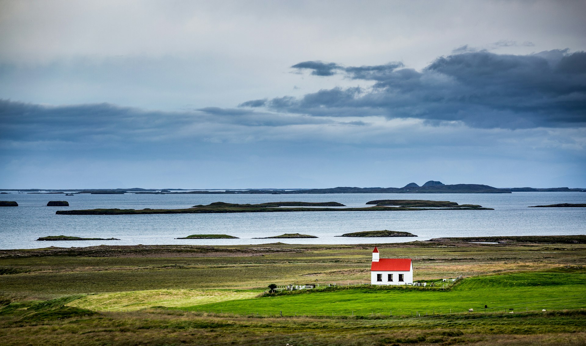 A house with a red roof in the middle of an otherwise empty green landscape with the sea in the background.