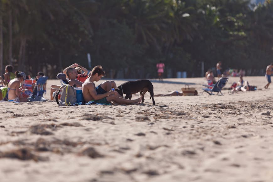 Grupper av människor och en hund ligger ute på sanden på stadsstranden i San Juan, Puerto Rico