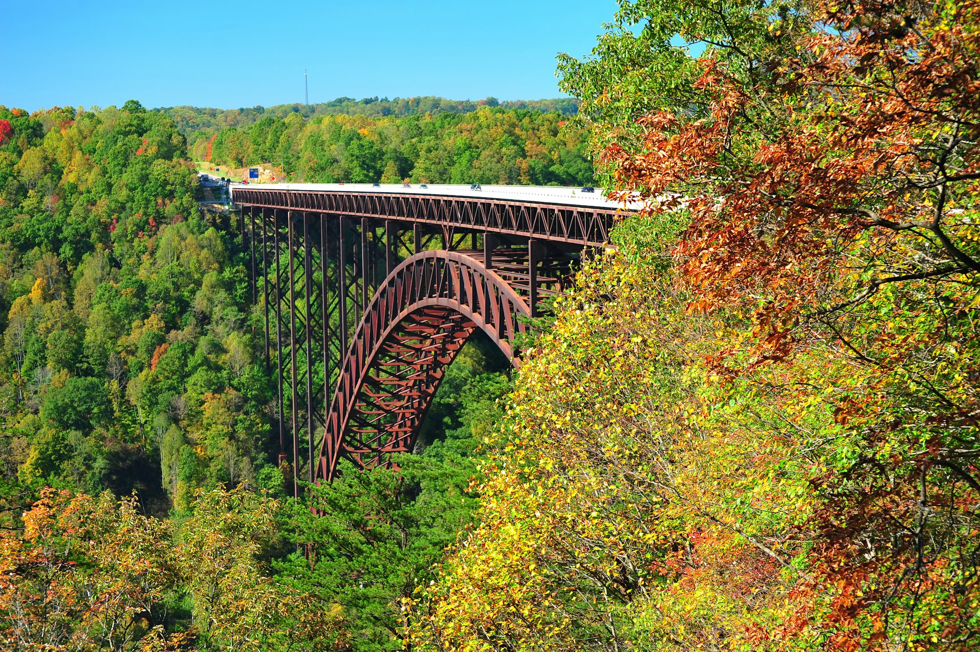 New River Gorge Bridge, seen between greenery and foliage beginning to turn colors