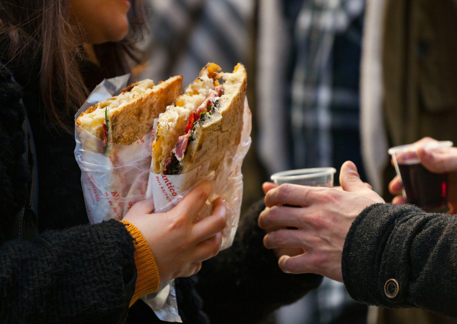 People holding large street-food sandwiches wrapped in paper