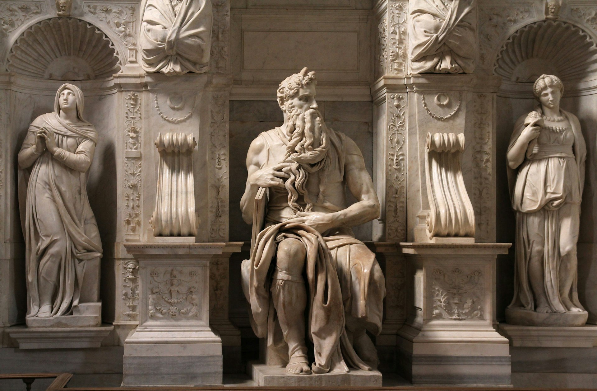 Michelangelo’s marble “Moses” sculpture, with a muscular pose and twisting beard, flanked by two niche sculptures