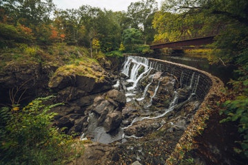 The thin streams of the waterfall are shot using the wide-angle lens, the skies are gloomy and the flora around is in dark warm colors, mostly green and yellow.
