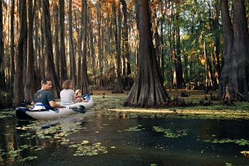Family in an inflatable boat floats among the cypresses. Caddo Lake State Park, Texas, United States